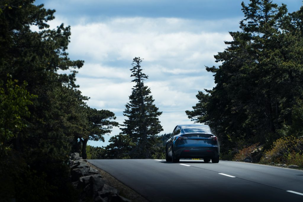 Midnight silver metallic Tesla Model Y driving down a road.